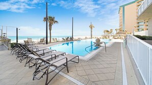 A pool area with lounge chairs and a view of the ocean.