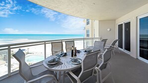 A balcony with a table set for two, overlooking a beach and pool.