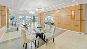 A modern hotel lobby with a round glass table, white upholstered chairs, wooden panel walls, and a chandelier.