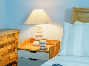 Uma mesa de cabeceira de madeira com uma luminária, uma xícara e uma gaveta.