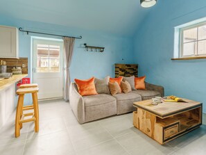Sala de estar com sofá, mesa de centro de madeira e área de cozinha com bancada e banquetas.