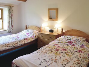 A room with two wooden beds, each with floral bedding and a wooden headboard. There are bedside tables with lamps and a small mirror on the wall.