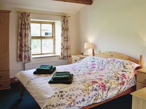 A bedroom with a floral bedspread, a wooden headboard, a nightstand with a lamp, and a window with curtains. - 2 bedroom accommodation in Gayle near Hawes (Gayle near Hawes)
