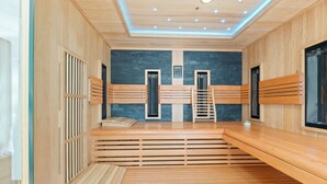 Ein Saunaraum mit Holzbänken, einer Steinwand und einer Decke mit eingelassener Beleuchtung.