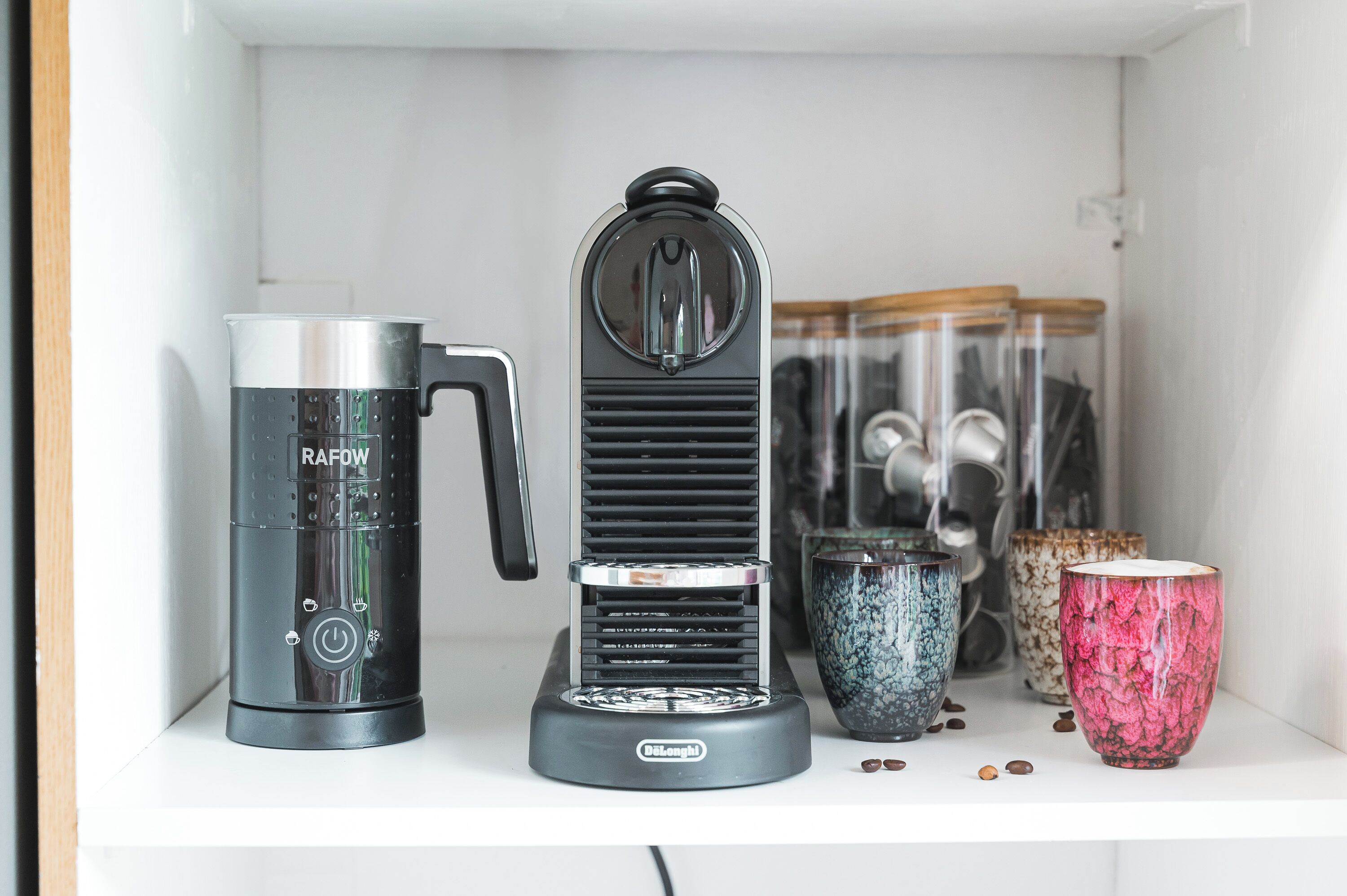 A kitchen area with a coffee maker, a blender, and decorative cups on a shelf.