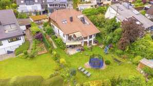 Ein Wohnhaus mit Ziegeldach, einem Balkon und einem Garten mit Trampolin.