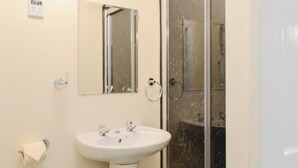Un baño con lavamanos blanco, un espejo y cabina de ducha con mampara de vidrio.