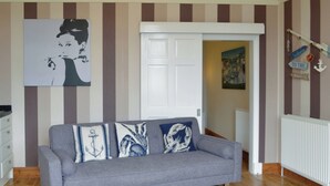 Un salón con un sofá gris, suelo de madera y un cuadro en la pared.