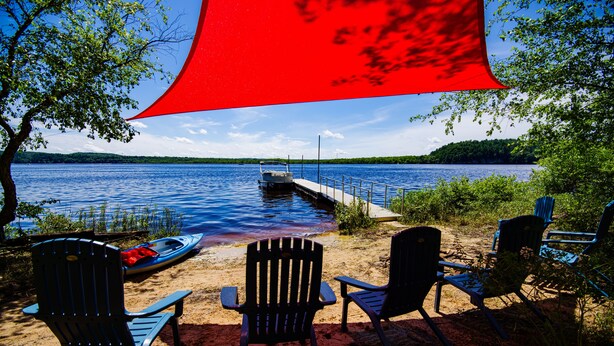 Um cenário à beira do lago com um píer, um barco canoe e várias cadeiras Adirondack.