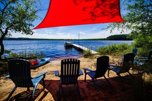 Eine Uferlandschaft mit einem Steg, einem Kanu und mehreren Adirondack-Stühlen.