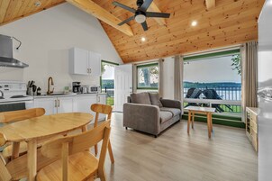 Une cuisine moderne avec des meubles blancs, une table à manger et des chaises. Une grande fenêtre offre une vue sur un lac, et un balcon est aménagé avec du mobilier d’extérieur.
