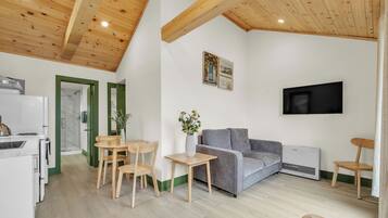 Un espacio habitable moderno con comedor, un sofá gris, un televisor de pantalla plana montado en la pared y una zona de cocina con horno empotrado.