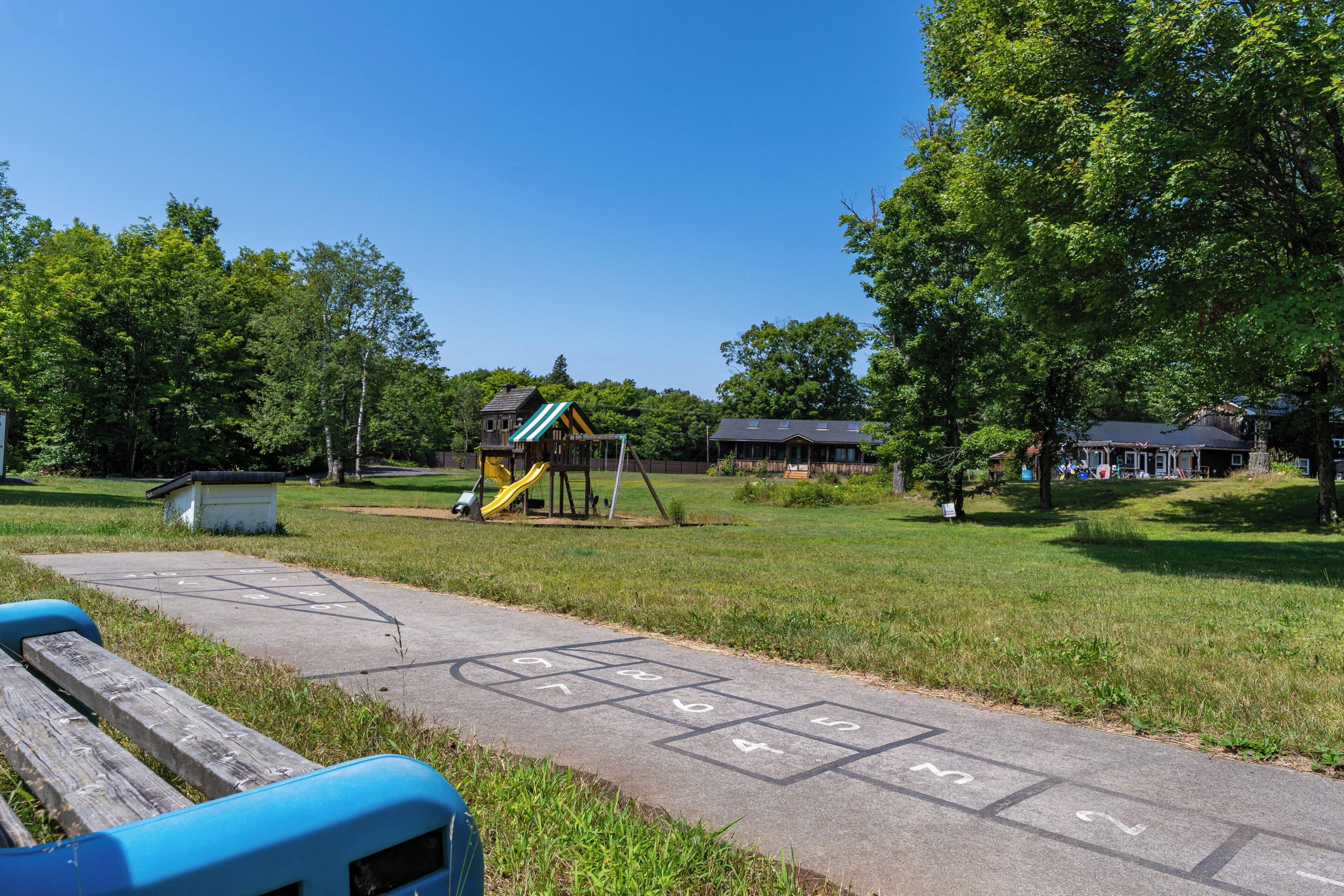 A park with a playground, a wooden bench, and a hopscotch game.
