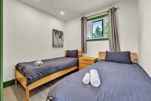 A twin room with two beds, a nightstand, a window with curtains, and a painting on the wall. - White Birches Cottages (Dwight)