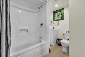 A modern bathroom with a bathtub, toilet, and a window with a green frame. - White Birches Cottages (Dwight)