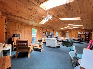 A cozy cabin with wooden walls, a ceiling fan, a fireplace, and a bookshelf.