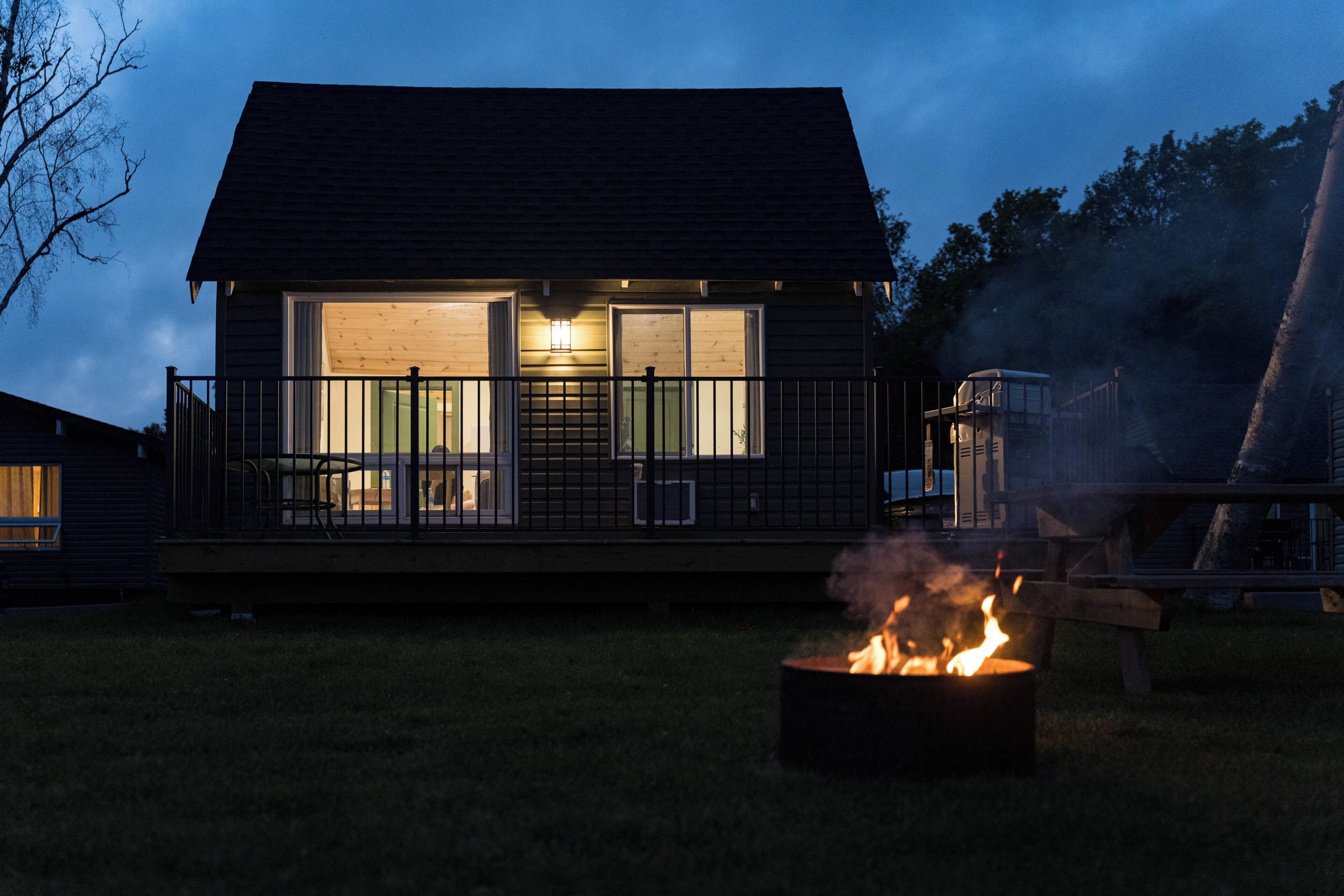 A cabin with a fire pit in the yard, a covered deck, and a large window.