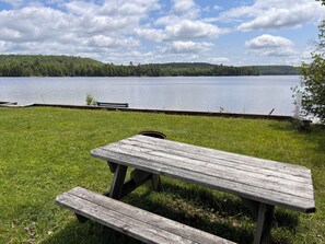 A picnic table with benches on a grassy area by a lake. - White Birches Cottages (Dwight)