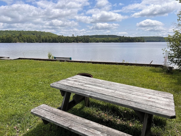 A picnic table with benches on a grassy area by a lake.