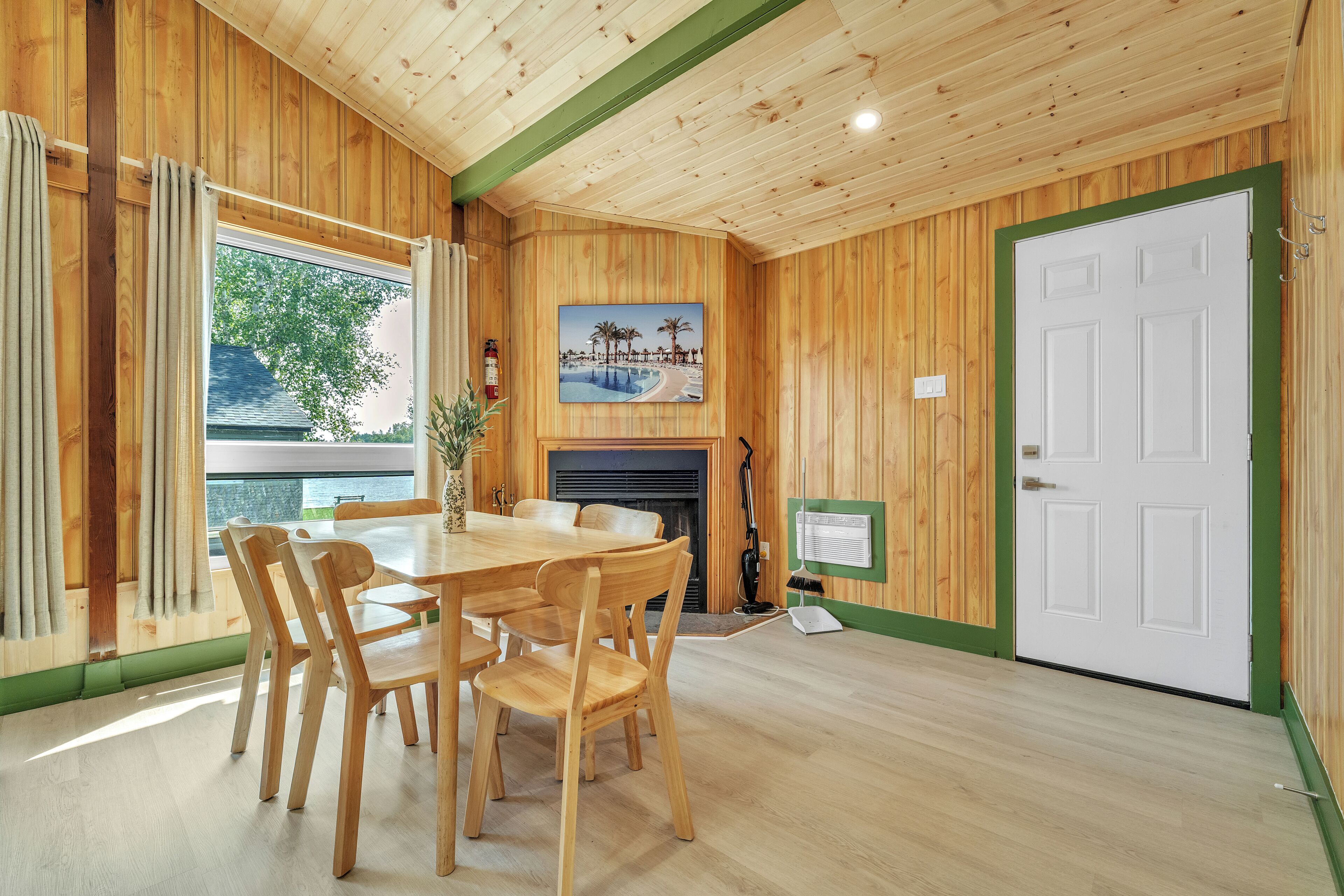 A room with a wooden interior, a dining table with chairs, a fireplace, and a door.