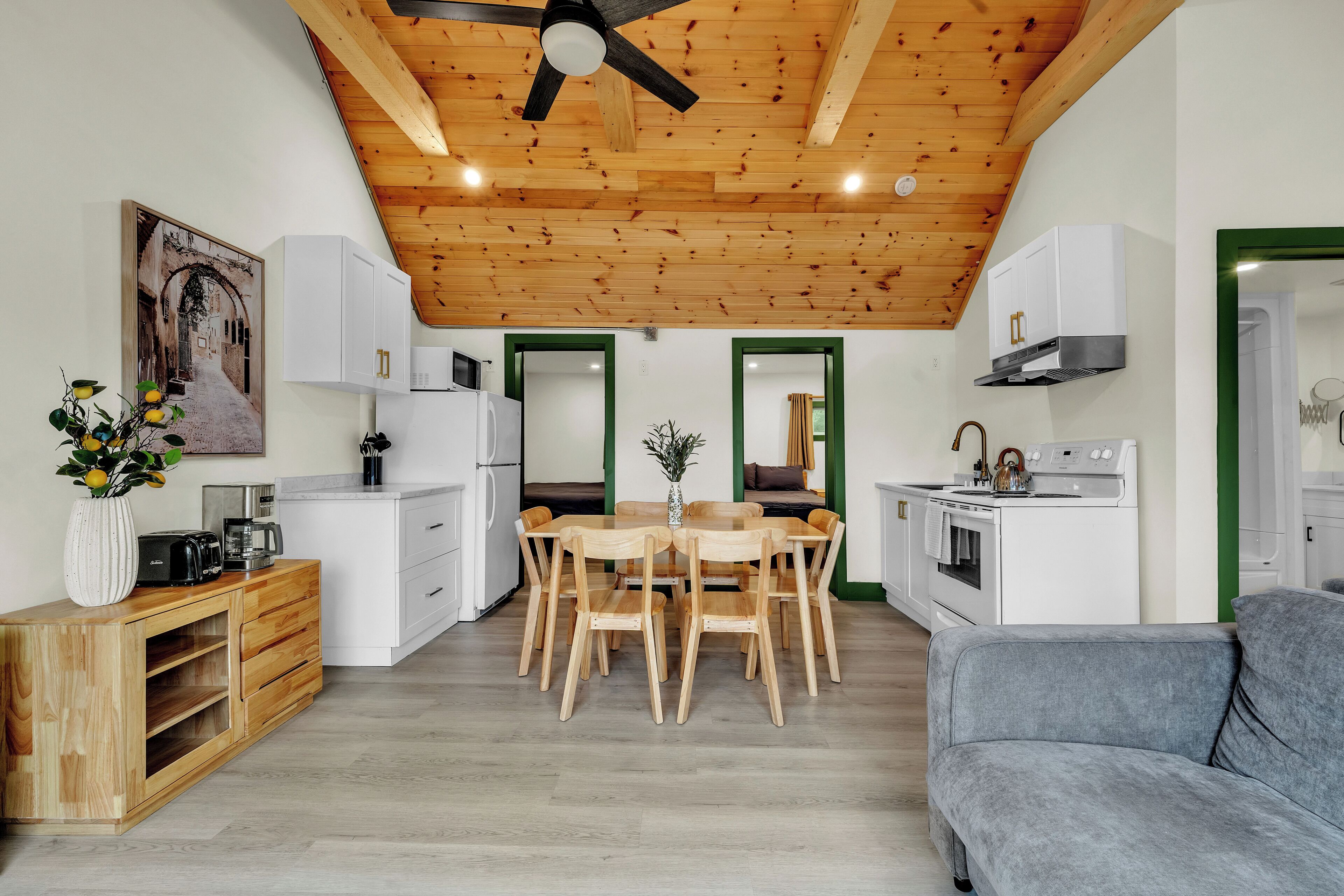 Una cocina moderna con vigas de madera en el techo, armarios blancos y un comedor con mesa y sillas de madera.