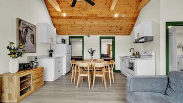 Una cocina moderna con vigas de madera en el techo, armarios blancos y un comedor con mesa y sillas de madera.