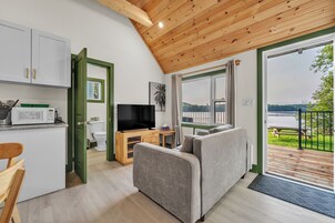 Un espacio habitable compacto con kitchenette, televisor, sofá y vista al lago.
