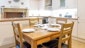 Una cocina moderna con armarios blancos, una mesa de comedor de madera dispuesta con platos y vasos, y una chimenea de ladrillo.