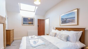 Un dormitorio con una cama grande, un cabecero de madera, un tragaluz, un radiador, un aparador de madera y dos cuadros en la pared.