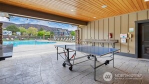An indoor pool area with a ping pong table, lounge chairs, and a view of houses and mountains. - Watershed Condo near Large pool/hot tub. Gorge Amp shuttle nearby book separate. (Quincy)