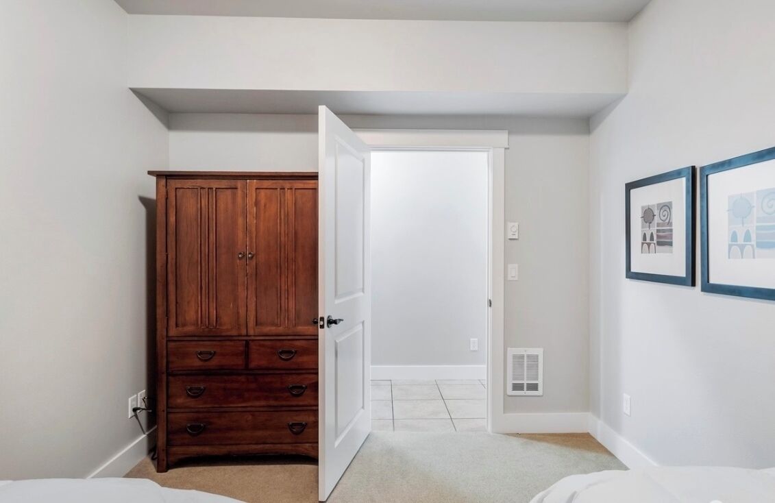 Een slaapkamer met een houten dressoir, een witte deur en twee ingelijste foto's aan de muur.