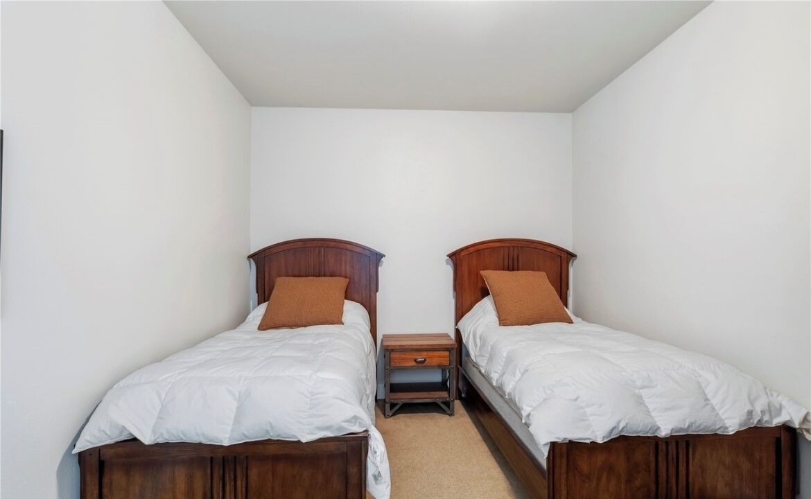 A small, clean room with two single beds, a nightstand, and a wooden headboard.