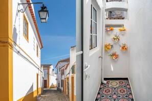 A narrow street with a cobblestone path, white buildings with yellow trim, and a door with a tiled floor.