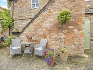 A brick building with a small patio area featuring wicker chairs, a round table, and potted plants.