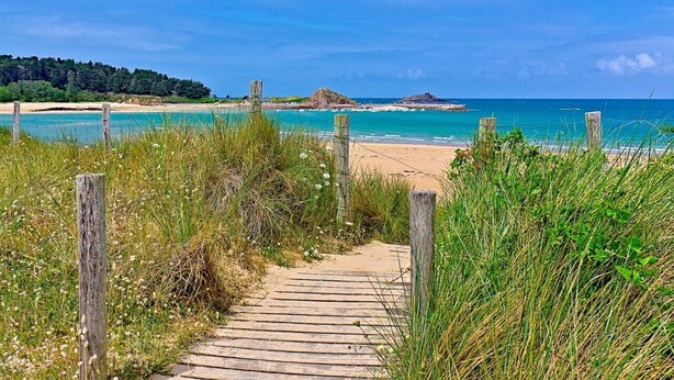 A wooden pathway leading to a beach with clear turquoise water and a sandy shore.