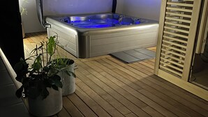 A hot tub with a wooden deck and potted plants.