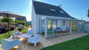 A modern house with a large glass-enclosed patio area, white furniture, and a well-maintained garden.