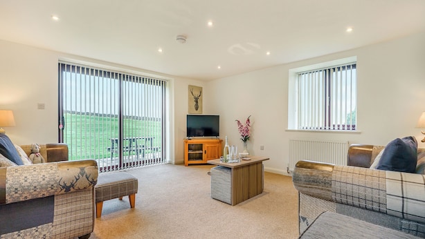A spacious living room with a large window, a television, and a wooden coffee table. - 2 bedroom accommodation in Whitby (Whitby)
