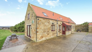 A stone building with a red-tiled roof, a paved courtyard, and a grassy area. - 2 bedroom accommodation in Whitby (Whitby)