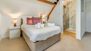A bedroom with a bed, nightstands, a lamp, a floral pillow, and a bathroom with a glass shower. - 2 bedroom accommodation in Whitby (Whitby)