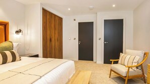 A bedroom with a bed, a wooden wardrobe, a dark door, a wooden chair, and a small table.