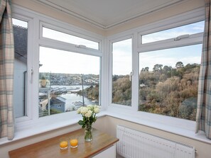 A bay window with a view of a town and a river, a vase with flowers, and two glasses of orange juice on a wooden ledge.