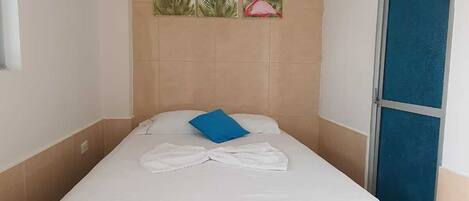 A single bed with a white mattress and a blue pillow, a wall-mounted air conditioner, and a door with a blue frame.