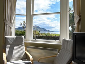 A room with two chairs facing a window overlooking a scenic landscape with hills and a body of water. - 3 bedroom accommodation in Lamlash, Isle of Arran (Lamlash, Isle of Arran)