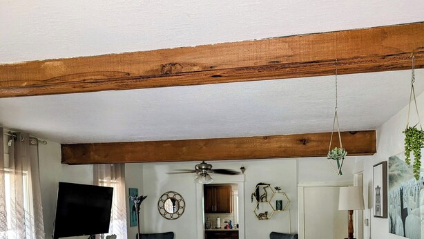 Een woonkamer met een houten plafond, een grijze bank, een televisie en een kamerbreed tapijt met een patroon.