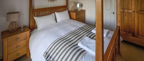 Un dormitorio con cama con dosel, cabecera de madera, mesitas de noche con lámparas y un armario.