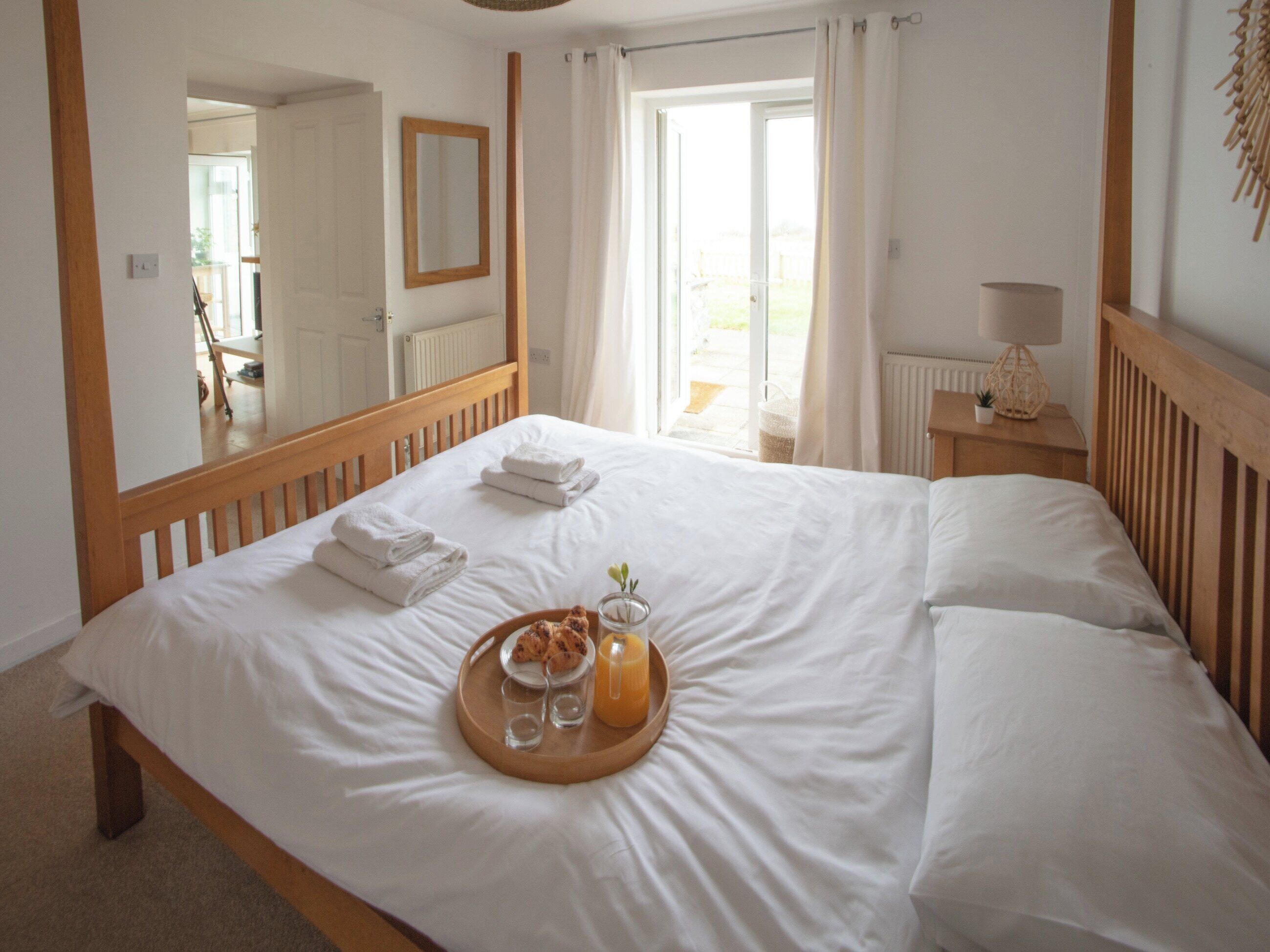 A neatly made bed with white linens, a tray with breakfast items, and a large mirror above it.
