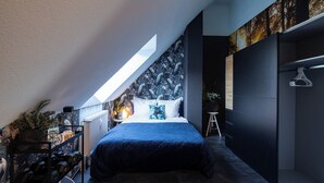 Ein Schlafzimmer mit Dachfenster, einem Bett, einem Heizkörper, einem kleinen Hocker und einem Kleiderständer.