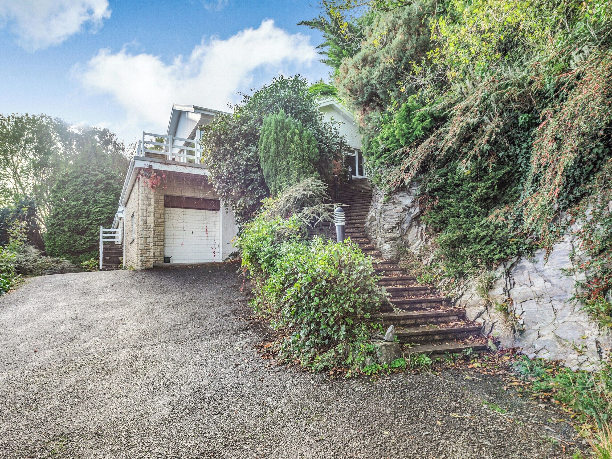 A stone building with a garage, a gravel driveway, and a staircase leading up to a house.