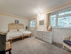 Een slaapkamer met een tweepersoonsbed, nachtkastje, spiegel, raam met gordijnen en uitzicht op bomen.